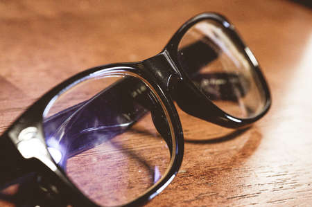 A closeup shot of a black framed glasses on a wooden tableの写真素材