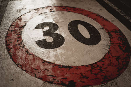 A weathered thirty mph street sign on an asphalt road