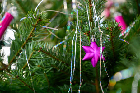 A closeup shot of a small pink star-shaped ornament on the Christmas tree with blurred background