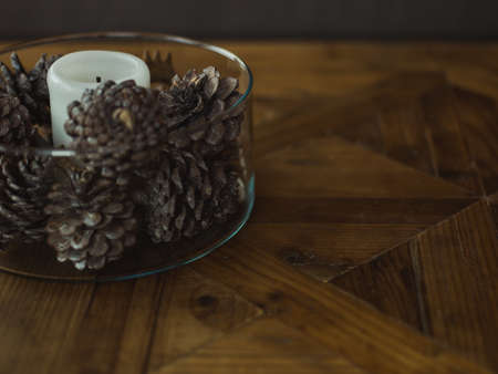 A closeup shot of a small white candle and cones in a glass jar on a wooden surfaceの写真素材