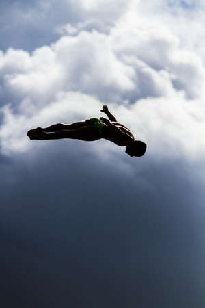 A vertical shot of a male jumping into the air with a blurred sky in the backgroundの写真素材