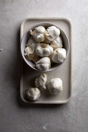 A vertical shot of a bowl with a lot of garlic on a white tray