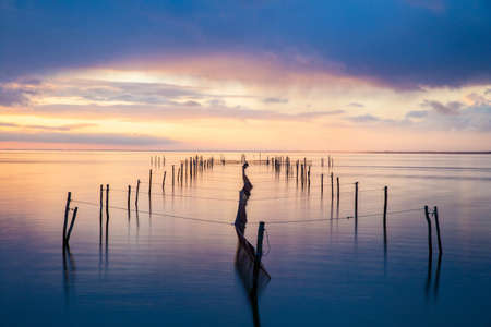 The wooden docks in the ocean with the reflection of light of the sunset in the pastel skyの写真素材