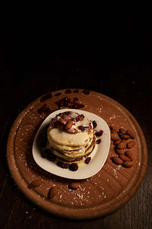 A vertical high angle shot of a stack of pancakes with white syrup and almonds on top on a wooden tray covered with baking powderの写真素材