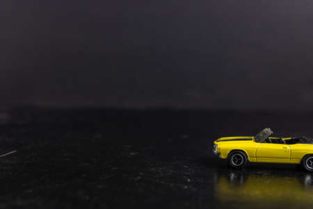 A selective focus shot of a yellow toy car with black stripes on a black surfaceの写真素材