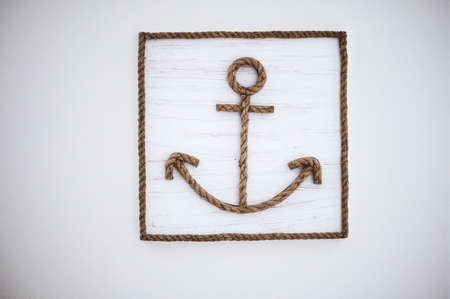 An anchor sign made from ropes on a white wooden wall
