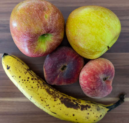 A high angle shot of a banana, apples, and Saturn peaches on a wooden surface