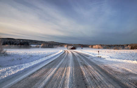The road near the forest covered with snow in winter under the cloudy skyの写真素材