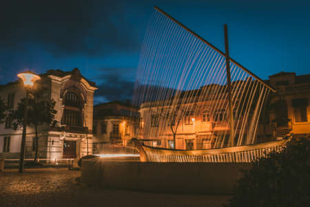 A fountain surrounded by lamps and buildings under a cloudy sky during the evening in Esposende