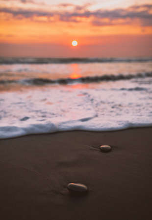 A beach with stones on it surrounded by the sea under a cloudy sky during a beautiful sunset