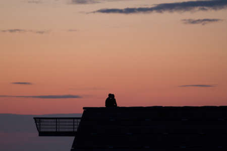 A silhouette of a romantic couple kissing on the roof during sunsetの写真素材