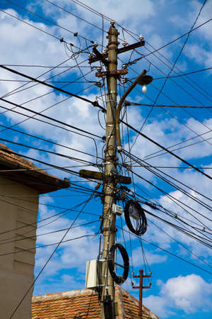 A vertical low angle shot of a lot of electricity wires under a cloudy skyの写真素材