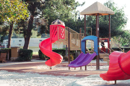 The colorful slides on the playground in a park with the trees in the background