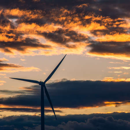 A windmill touching the warm firey sky during the evening time