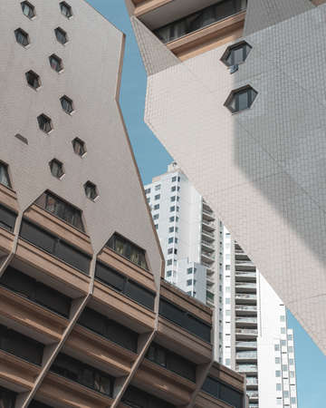 A vertical picture of white modern buildings under a blue sky and sunlight
