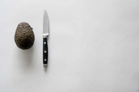 A high angle shot of a fresh delicious avocado with a knife on a white surfaceの写真素材