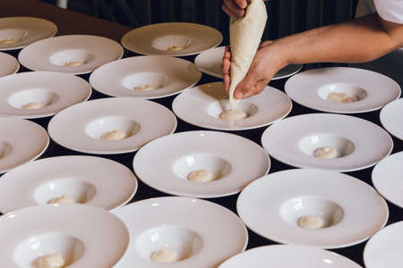 A cook adding some white cream in serving plates in a restaurant