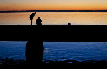 A silhouette of two friends arguing on a concrete bridge with the sunset in the backgroundの写真素材