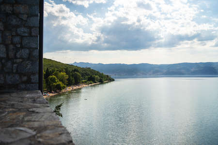 A sea surrounded by greenery and buildings with mountains under a cloudy sky on the backgroundの写真素材