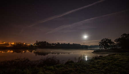 The moon shining in the sky full of stars and reflected in the lake below