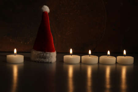 A holiday Santa hat and burning candle on a black surface