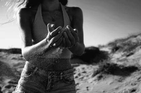 A greyscale shot of the sand sliding through the palms of a female