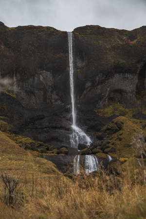 A waterfall surrounded by rocks and dry grass under a cloudy sky - a cool picture for wallpapers
