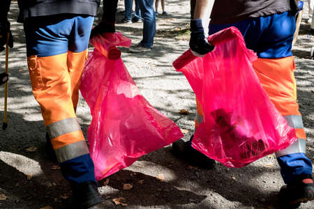 A low angle view of people in uniforms collecting rubbish in pink plastic bags