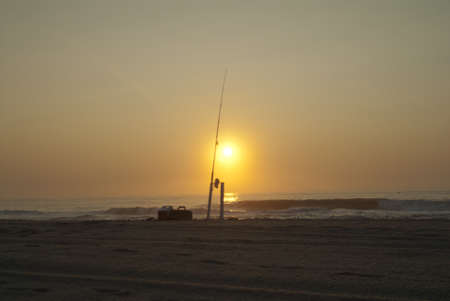 A landscape of a beach with a fishing rod on it surrounded by the sea during a beautiful sunset