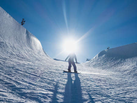 The light of the bright sun blinding the snowboarder standing in the snowy hillsの写真素材