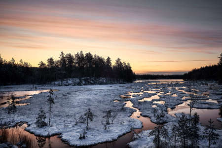 The snow formations on the lake reflecting the colors of the sunset sky