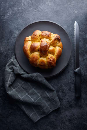 A vertical high angle shot of freshly baked pastry in a black plate near a knife on a black surface