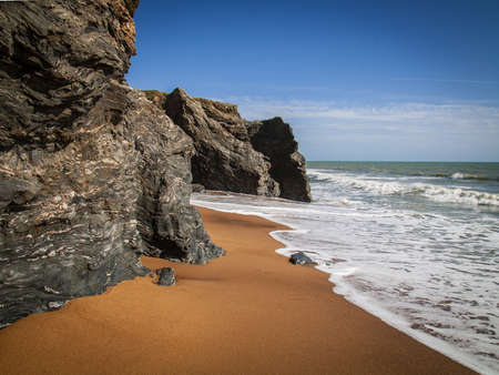 A beautiful shot of the seashore with dark cliffs and golden sand with the sun in the backgroundの写真素材