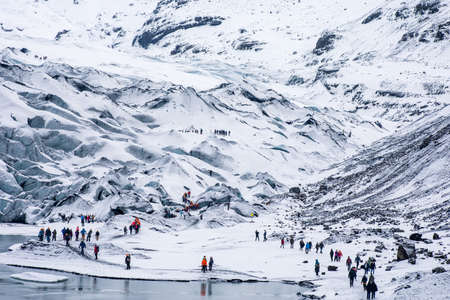 The groups of hiking tourists trekking in the snowy white rugged mountainsの写真素材