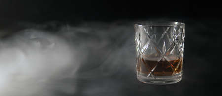 A glass of whiskey on a table covered with smoke against a black backgroundの写真素材