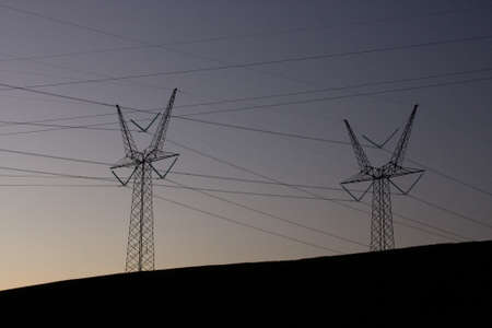 A silhouette of electric towers with a dark blue sky in the background