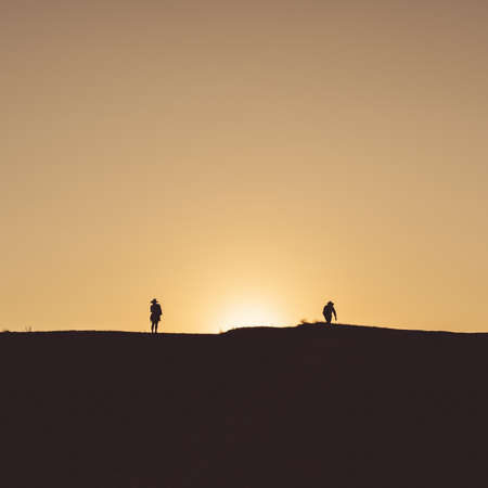 The small silhouettes of people walking on the land with with the yellow sunset sky in the backgroundの写真素材