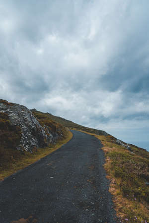 A vertical shot of a road on the hill with nobody walking under the cloudy skyの写真素材