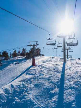 A vertical shot of the sun shining in the sky over the snowy mountain with cable carsの写真素材