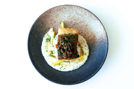 A high angle shot of grilled fish with white cream in a black plate on a white surfaceの写真素材