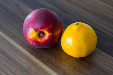 A closeup shot of a nectarine and a tangerine on a wooden surfaceの写真素材