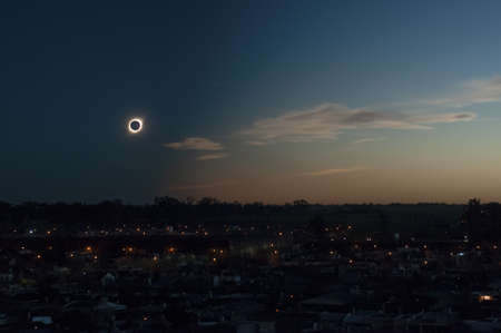 A total solar eclipse during the evening above a modern town surrounded by buildings trees and...