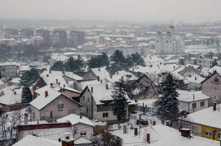 A high angle view of a town with buildings and trees covered in the snow and fogの写真素材