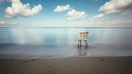 A wooden chair standing at the ocean shore under the sunlight reflecting  in the waterの写真素材