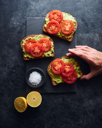 A high angle shot of a person taking an avocado toast on a black surface