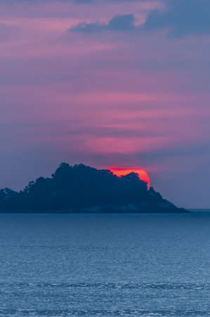 A vertical shot of a  breathtaking sunset scenery with the sun going down the hills in the Patong...