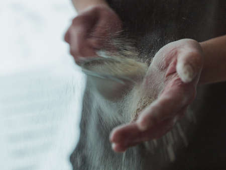 A closeup shot of the cook pouring powdered sugar with a strainer on blurred backgroundの写真素材