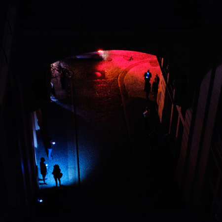 A high angle shot of some people standing under the colorful lights in a dark alley at night