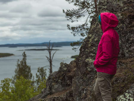 A person in a pink raincoat standing near the rocks and looking at the lake belowの写真素材