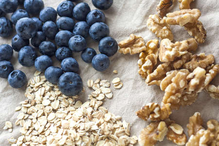 A high angle shot of some blueberries, oatmeal and walnuts on a white table clothの写真素材